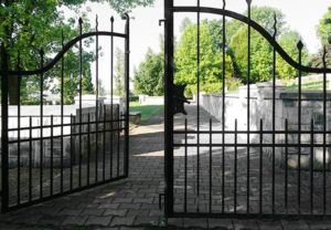 Wrought iron gate halfway open with stone pathway and green trees